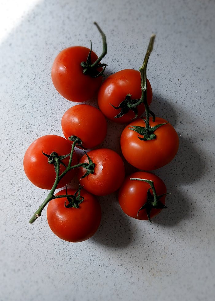 Cluster of ripe red tomatoes on a light speckled countertop, showcasing natural textures.